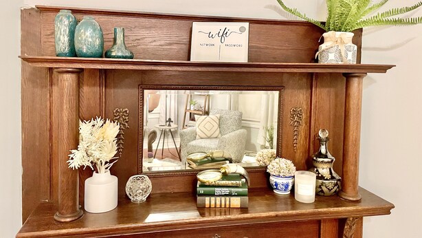 A wooden mantelpiece with decorative items, a framed mirror, and a sign with 'wifi' and 'password' visible. - Cozy Getaway | Splendid Historic Thibodaux Gem (Thibodaux)