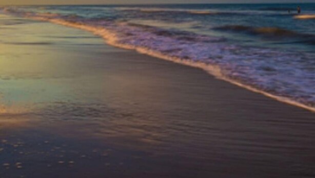 Ein Strand mit Wellen, blauem Himmel und Sonnenuntergang.