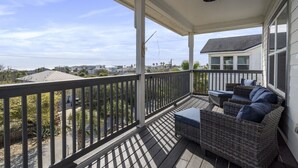 Eine überdachte Veranda mit Blick auf das Meer, Korbmöbel und ein Deckenventilator.