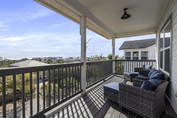 A covered porch with a view of the ocean, wicker furniture, and a ceiling fan.