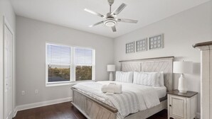 Ein Schlafzimmer mit Bett, Nachttischen, Deckenventilator, Fenster mit Jalousien und Blick ins Grüne.