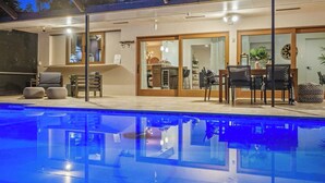 A modern outdoor pool area with a dining setup and a kitchen visible through glass doors. - Family Beach Villa w/ Home Theater & Heated Pool! (Hollywood)