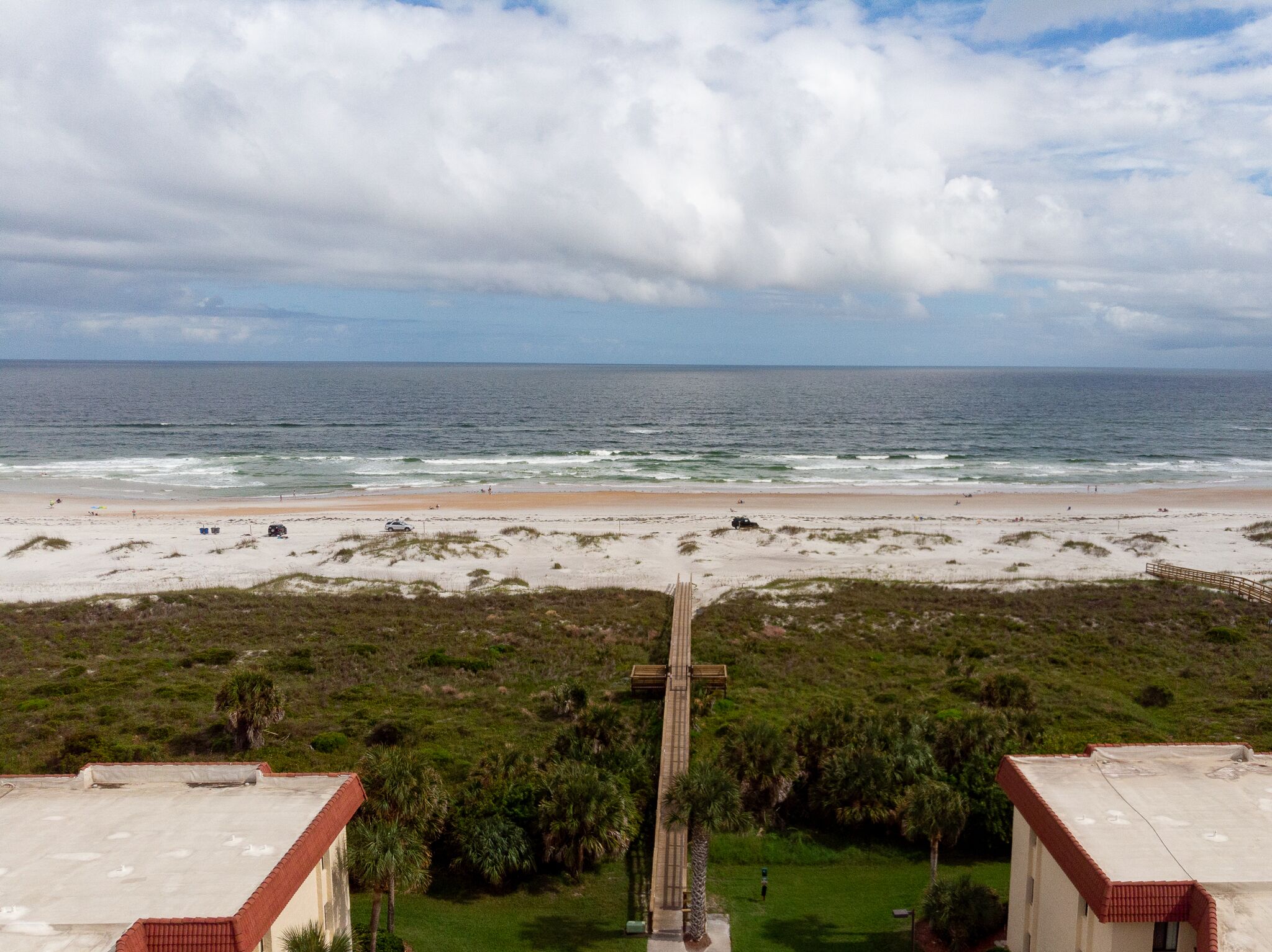 A beach with a wooden cross, grassy dunes, and a view of the ocean.