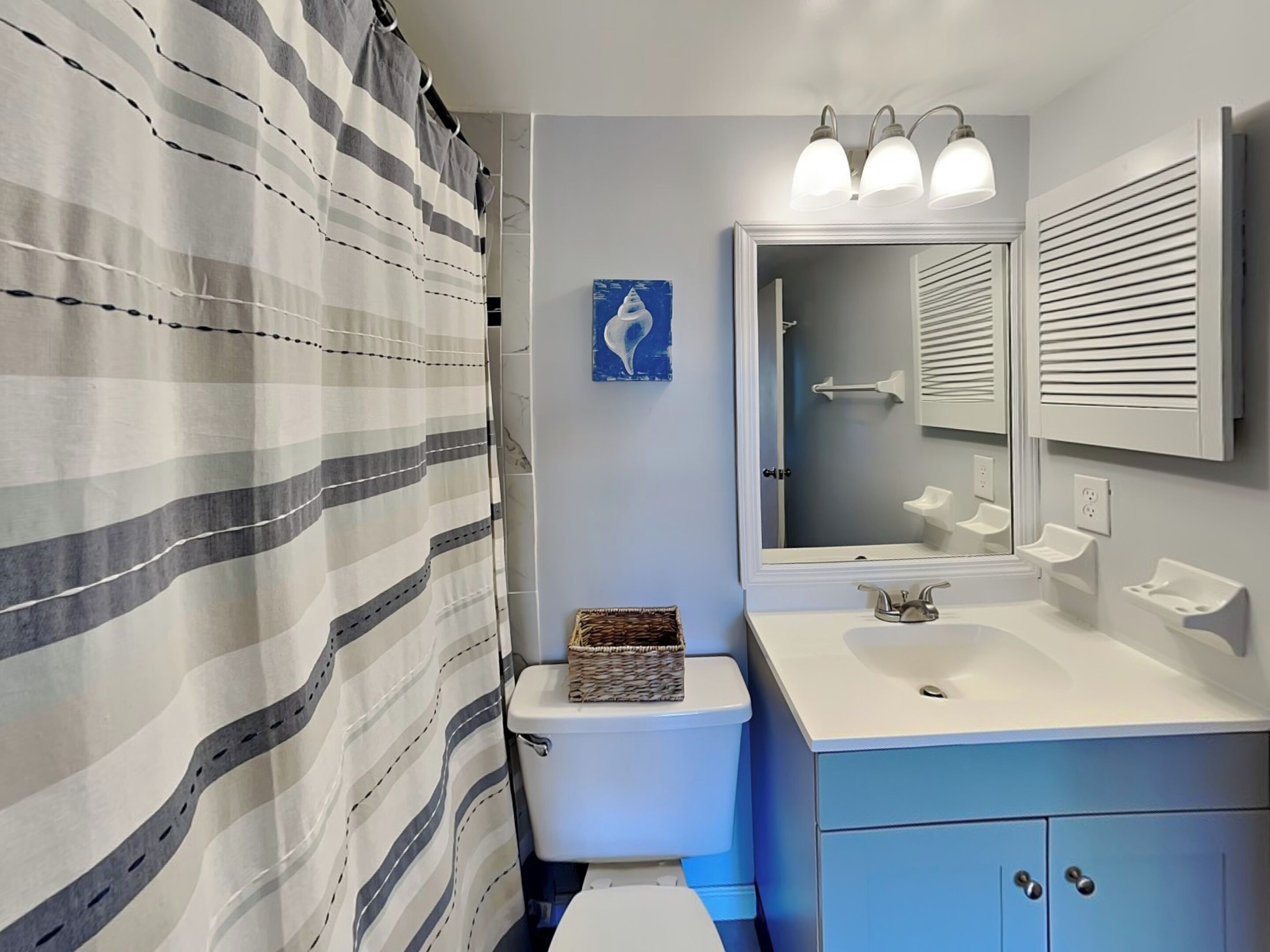A bathroom with a striped shower curtain, a toilet, a sink with a mirror, and a wall-mounted light fixture.