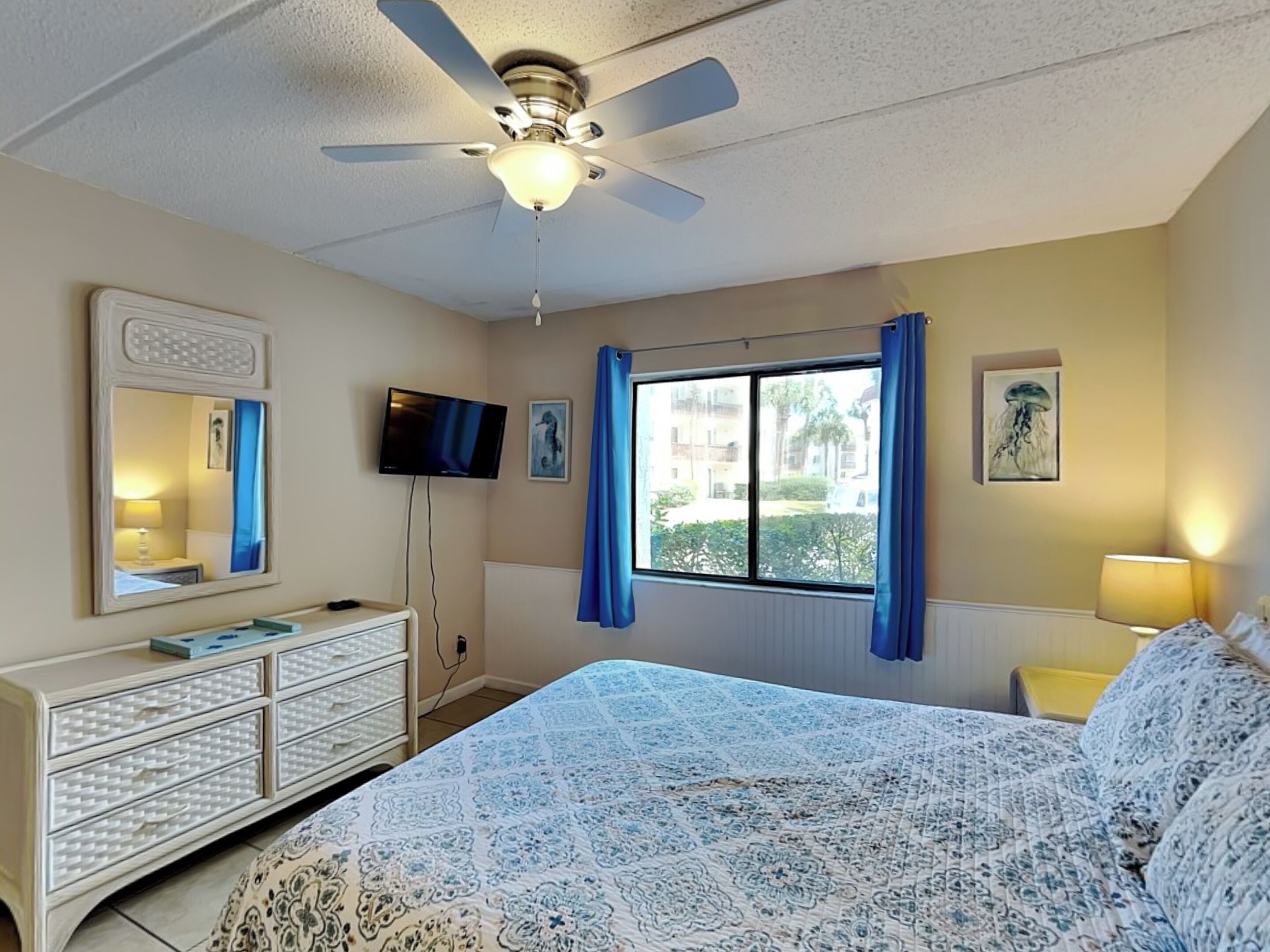A bedroom with a bed, a dresser, a television, and a window with curtains.