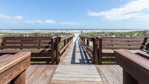A wooden boardwalk leading to a beach with benches on either side.