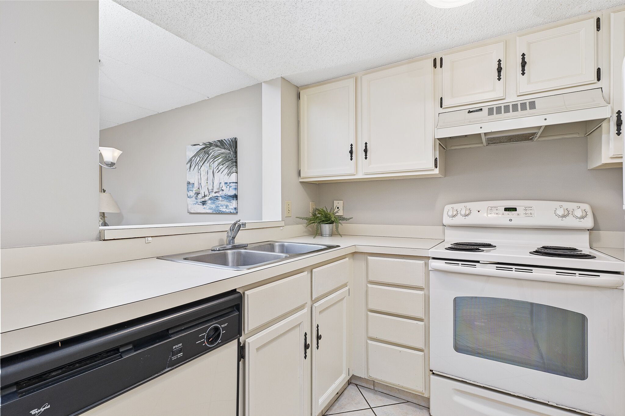 A compact kitchen with white cabinets, a dishwasher, a stove, and a sink.