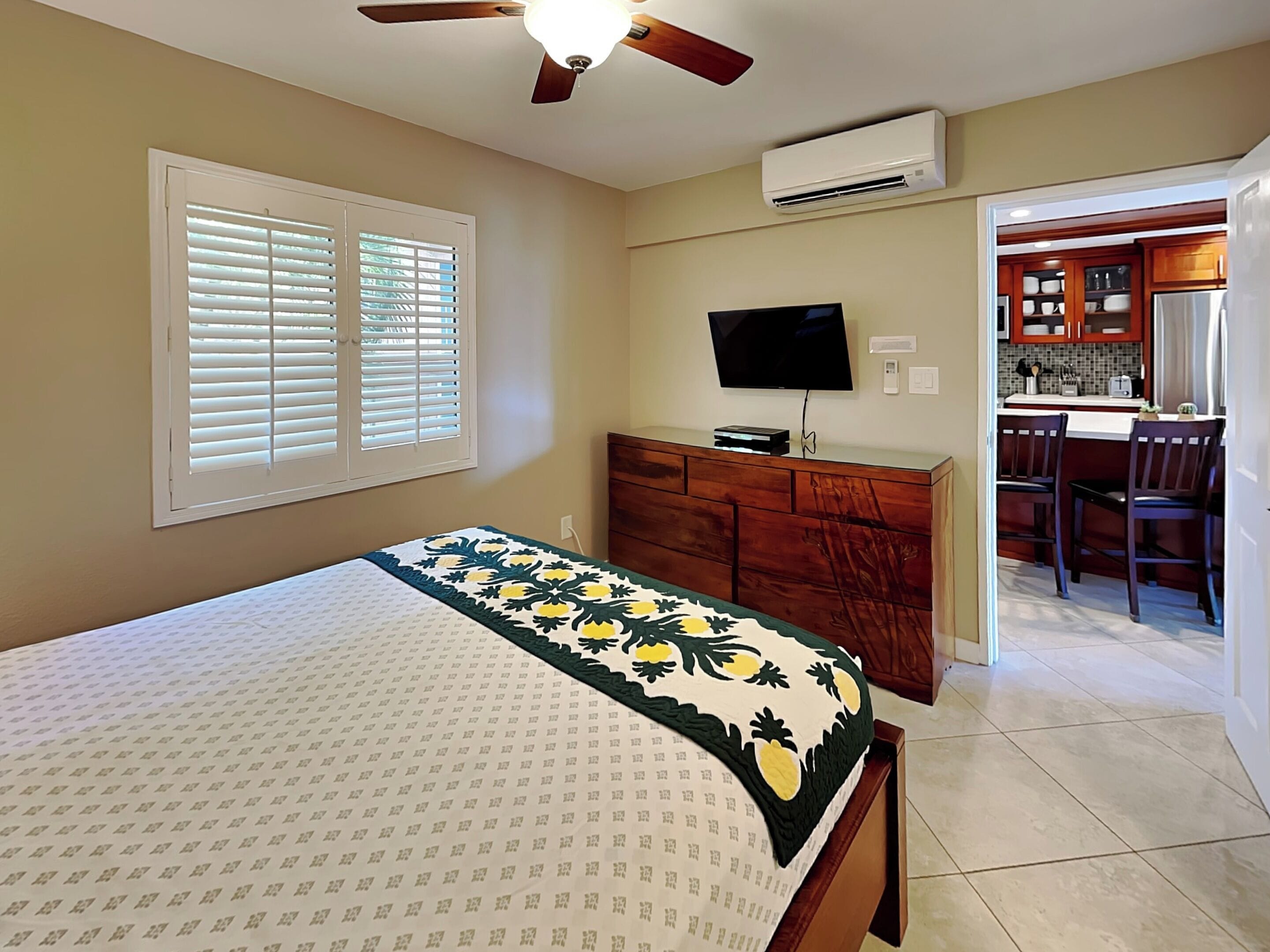 A bedroom with a bed, a TV, a ceiling fan, and an air conditioner.
