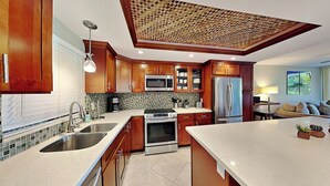 A modern kitchen with wooden cabinets, stainless steel appliances, and a large island. - Pacific Shores by Maui Rental Group (Kihei)