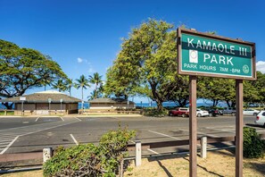 A parking lot with a sign for Kamaole III Park, indicating park hours from 7 AM to 8 PM. - Pacific Shores by Maui Rental Group (Kihei)