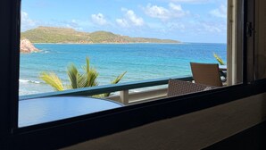A room with a view of the ocean and hills, a window with a view, and a chair with a cushion. - Discover Your Island Oasis: St. Thomas Condo (St. Thomas)