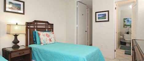 Une chambre à coucher avec un lit, une table de chevet et une lampe. Une porte donne accès à la salle de bain.