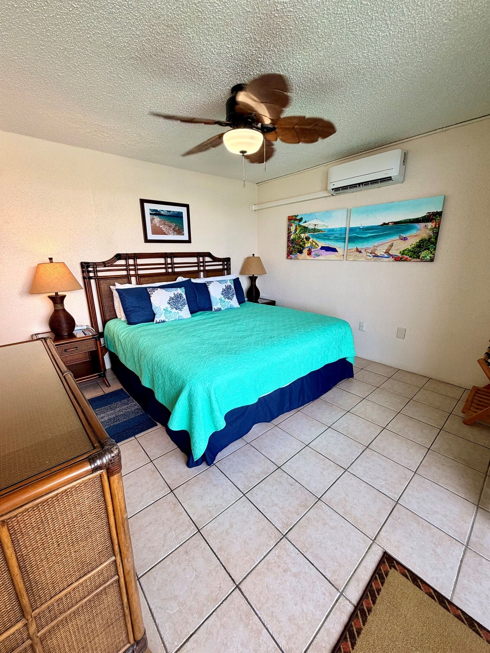 Ein Schlafzimmer mit Bett, Deckenventilator, Klimaanlage und Strandmotiven an der Wand.