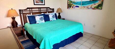 Ein Schlafzimmer mit Bett, Deckenventilator, Klimaanlage und Strandmotiven an der Wand.