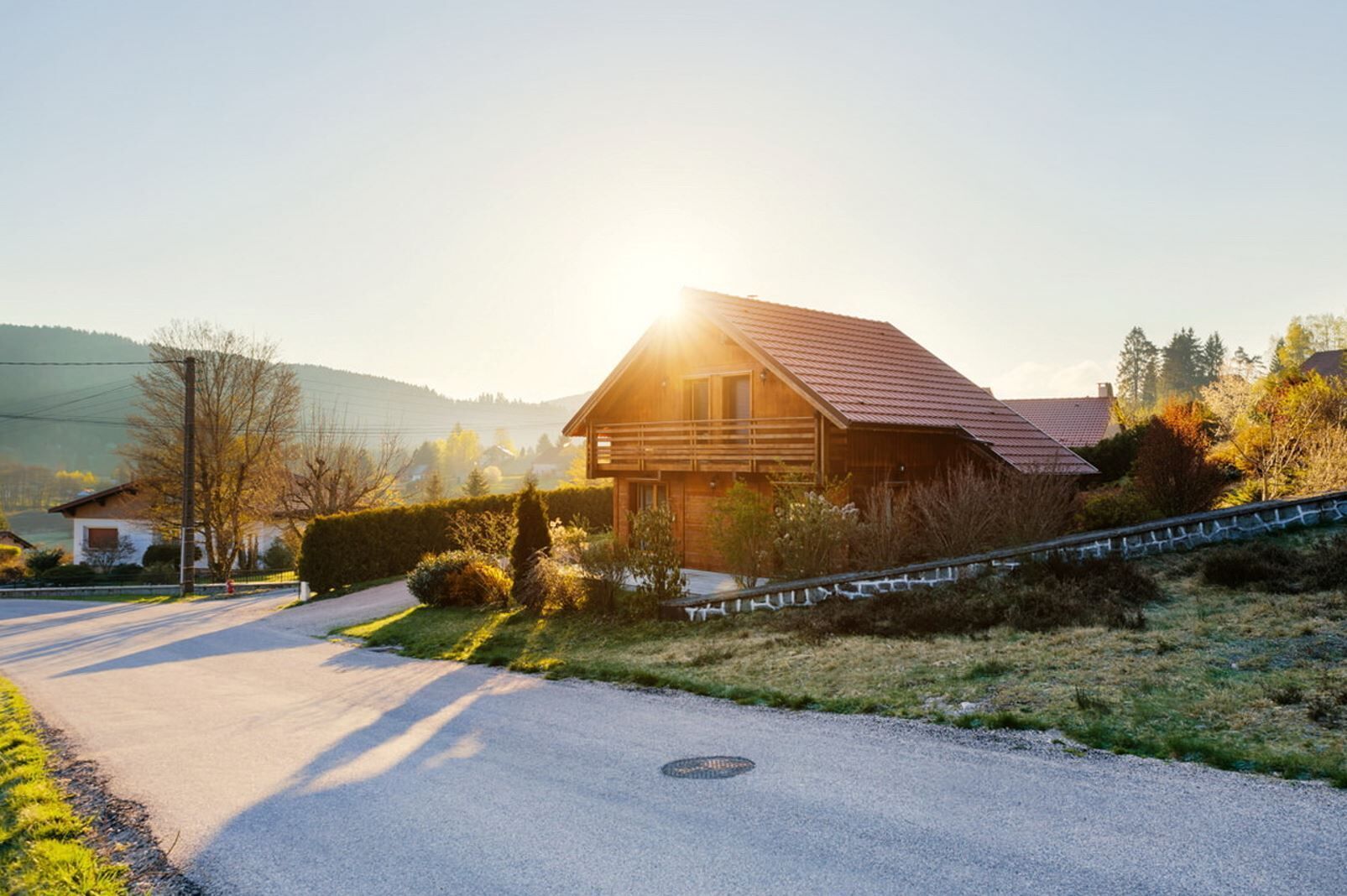 Une maison en bois avec un toit rouge, entourée d’un jardin bien entretenu et d’une allée gravillonnée.