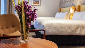 A hotel room with a bed, a bedside table with a vase of flowers, a chair, and a lamp. - Wigram Hotel (Christchurch)