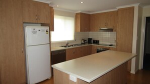 A kitchen with wooden cabinets, a refrigerator, a sink, and a stove.