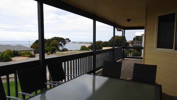 A covered outdoor area with a table and chairs, overlooking a body of water and a residential area.