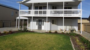 A two-story house with a balcony on the upper floor, a front door, and a small front yard with plants.