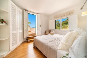 Ein Schlafzimmer mit Bett, einem Fenster mit Aussicht, einer Tür, die auf einen Balkon führt, und einem weißen Kleiderschrank.