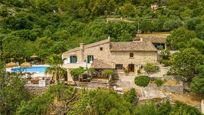 A stone villa with a swimming pool, surrounded by lush greenery and hills.