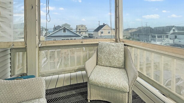 Un balcon abrité, agrémenté d’une chaise en osier et d’un banc rembourré, donnant sur un quartier résidentiel avec des maisons et un ciel dégagé.