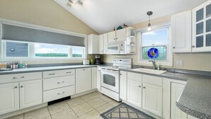 Une cuisine avec des meubles blancs, une cuisinière, un four à micro-ondes et une fenêtre donnant sur un paysage verdoyant.