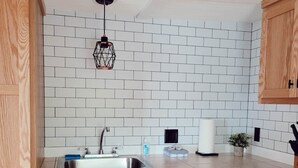 A kitchen with wooden cabinets, a white tiled backsplash, a stainless steel sink, and a hanging pendant light. - Cabin 2 | Headwater (Nevis Township)
