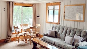A cozy living room with a wooden bench, a patterned sofa, and a dining area with a table and chairs. - Cabin 2 | Headwater (Nevis Township)