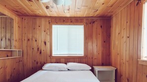 A wooden-paneled room with a bed, a window with blinds, and a small bedside table.