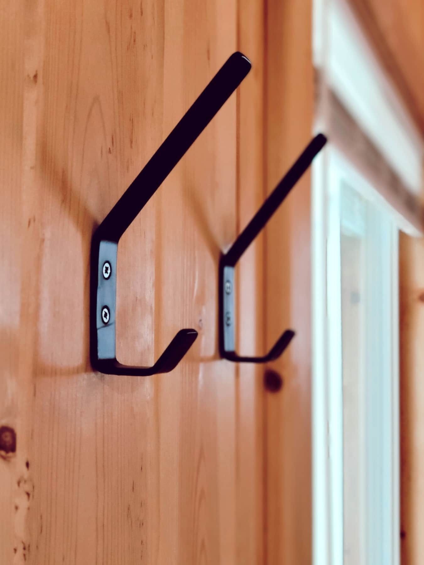 Deux crochets en métal noir fixés à un mur en bois.
