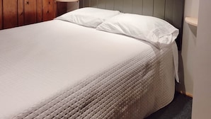 Un lit bien fait, avec du linge de lit blanc, dans une pièce dont les murs et le plafond sont recouverts de lambris en bois.