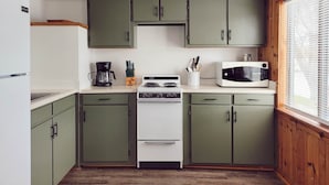 Une cuisine de taille réduite avec des meubles de couleur verte, une cuisinière, un four à micro-ondes et une machine à café.