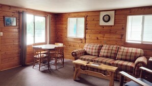 A cozy cabin interior with a plaid sofa, a wooden table, and a dining table with chairs.