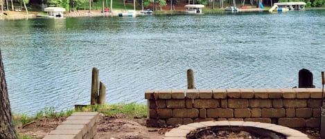 A lakeside view with a fire pit and a brick wall.