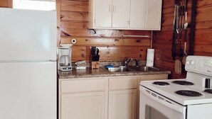 A compact kitchen with wooden walls, a white refrigerator, a stove, and a sink.