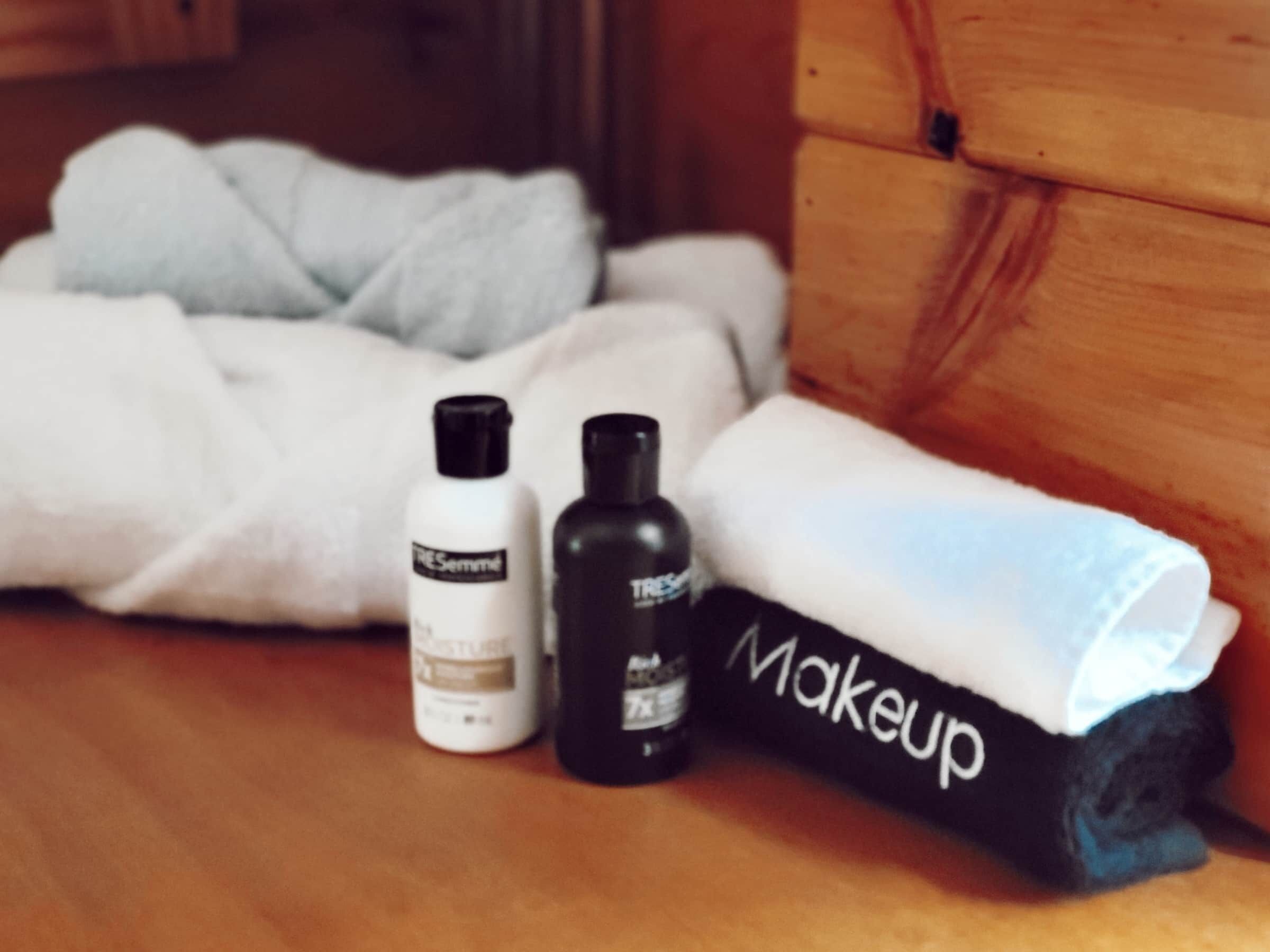 Une boîte en bois contenant une serviette enroulée étiquetée « Maquillage » et deux flacons de produits de soins pour la peau, le tout posé sur une surface en bois.