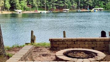 A lakeside view with a fire pit and a brick wall.