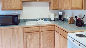 A kitchen with wooden cabinets, a microwave, a coffee maker, and a sink. - Cabin 8 | Northwoods (Nevis Township)