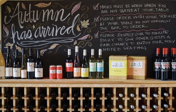 A wine rack with various bottles and a chalkboard with 'Autumn has arrived' written on it.