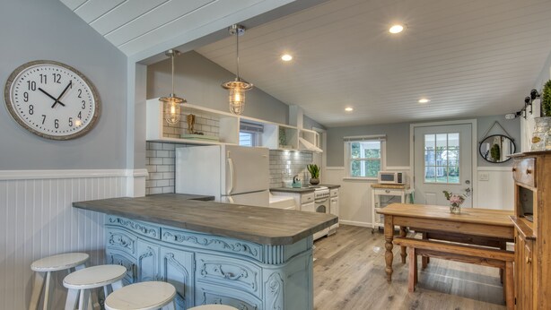 A kitchen with a central island, bar stools, a dining table, and a clock on the wall. - Modern Farmhouse Steps to Beach and Love Lane  (Mattituck)