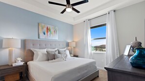 Ein Schlafzimmer mit einem Bett, zwei Nachttischen, einem Deckenventilator, einem Fenster mit Vorhängen und Blick ins Freie.