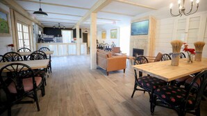 Un espace repas avec des tables et des chaises en bois, une cheminée et une cuisine en arrière-plan.