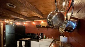Une cuisine compacte aux murs en bois, avec un réfrigérateur noir, un évier et des casseroles suspendues.