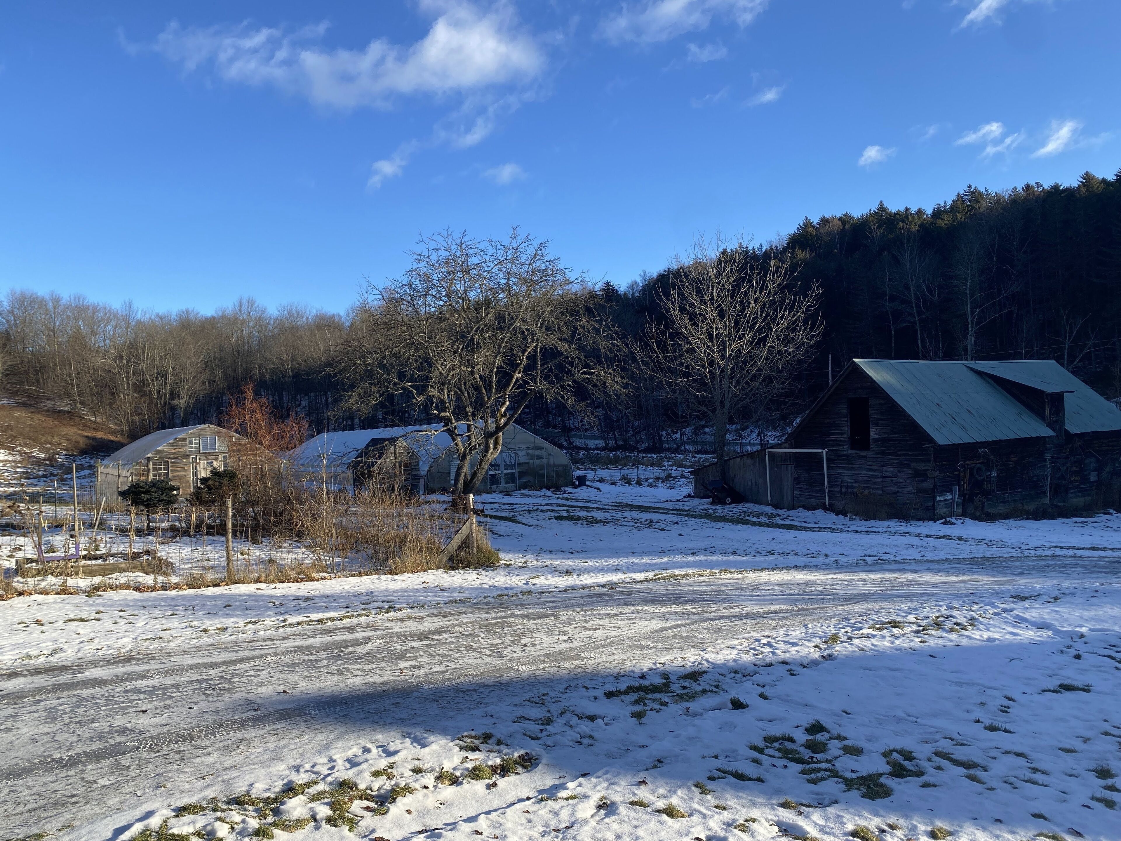 Ländliche Landschaft mit Scheune, Gewächshaus und schneebedecktem Feld.