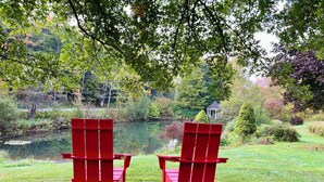 Zwei rote Adirondack-Stühle, die auf einen Teich blicken, mit einem Gazebo im Hintergrund.