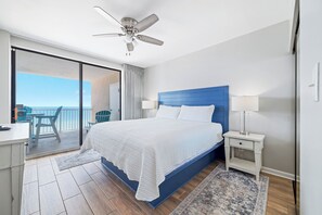 Une chambre avec un grand lit, un ventilateur de plafond, une table de chevet et une vue sur le balcon.