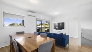 A modern living space with a wooden dining table, blue sofa, and a flat-screen TV mounted on the wall. - Top Town Terrace - short walk to town center (Woolgoolga)