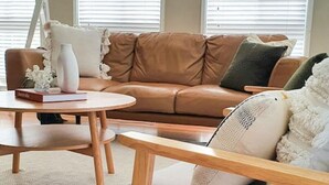 A living room with a brown leather sofa, a round wooden coffee table, and a grey armchair with a white throw blanket.