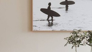 A dining area with a wooden table, black chairs, and a framed picture of surfers on a beach.
